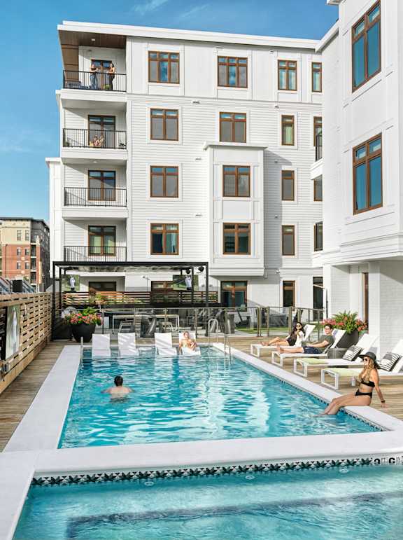 A group of people are enjoying the pool at a white apartment building.