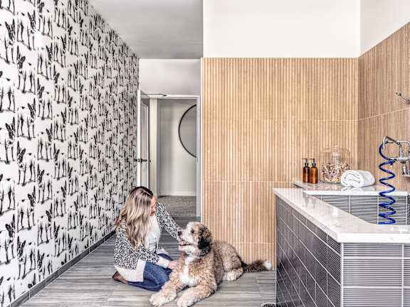 A woman is sitting on the floor with her dog in a bathroom.