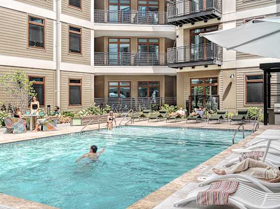 A person swims in a pool surrounded by lounge chairs.