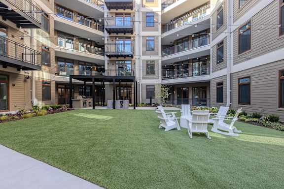 A large grassy area with four white chairs in front of apartment buildings.
