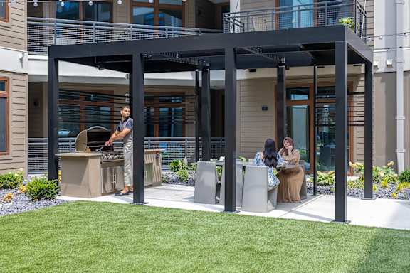 A man grilling food on a patio with two women sitting at a table.
