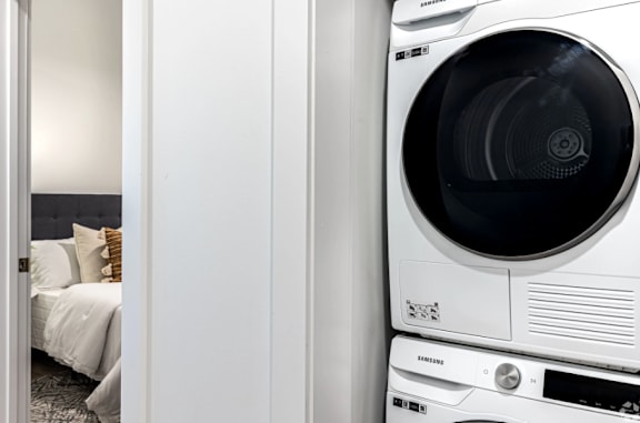 A white Samsung washing machine is placed next to a bed.