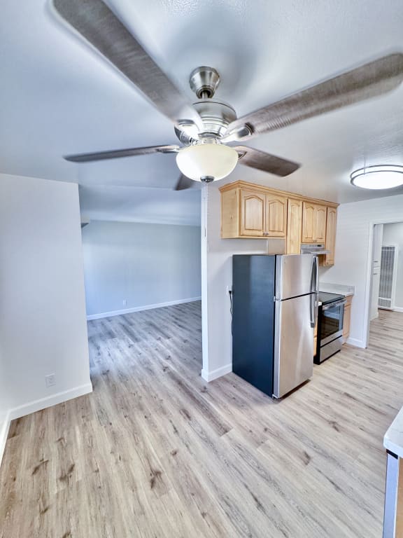 an empty living room with a ceiling fan and a refrigerator