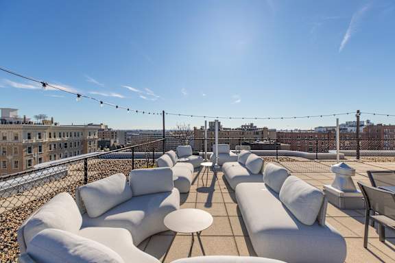 A rooftop patio with white couches and tables.