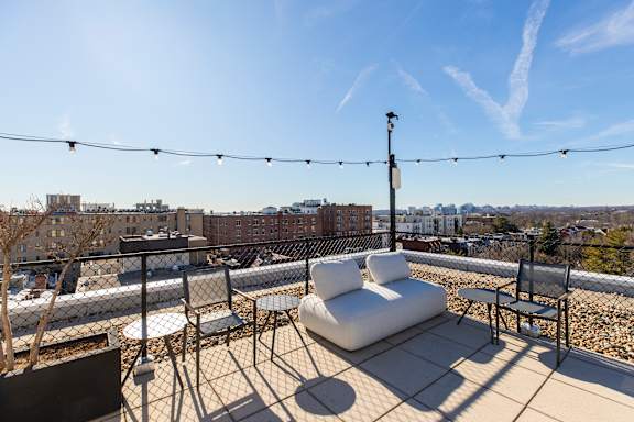 A rooftop patio with white furniture and string lights.