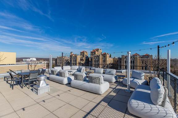 A rooftop patio with white furniture and a view of buildings in the distance.