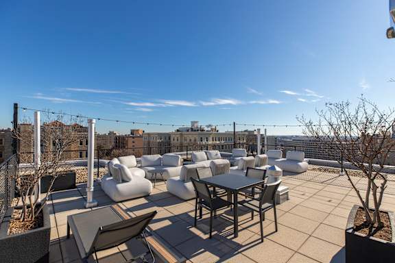 A rooftop patio with white furniture and a view of the city.