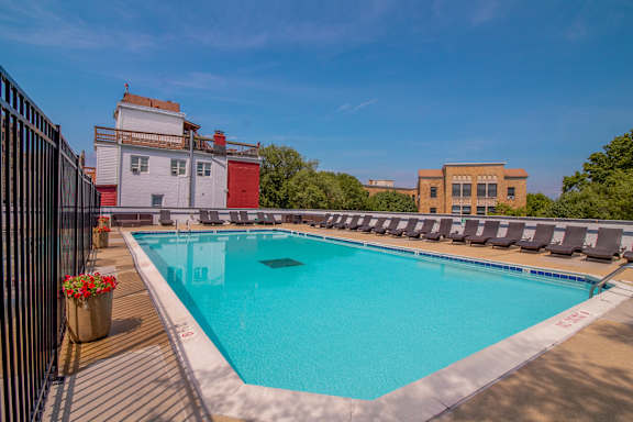 A large outdoor swimming pool surrounded by lounge chairs and buildings.