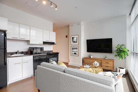 A modern living room with a grey sofa and a kitchen area with white cabinets.