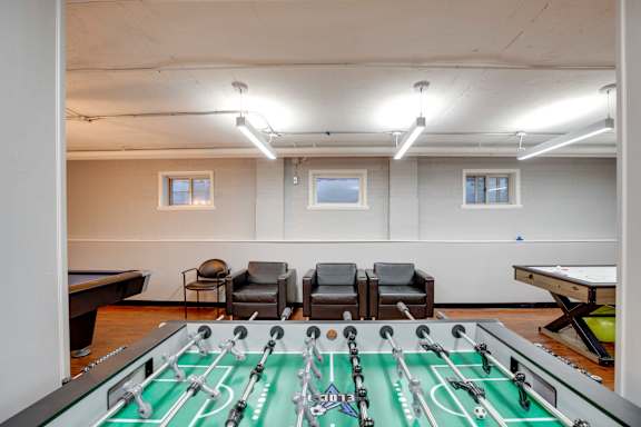 A foosball table is in the middle of a room with a pool table and chairs.