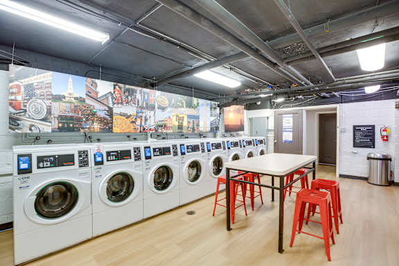 A laundromat with a row of washing machines and a table with stools.