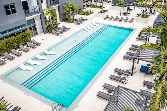 A large swimming pool surrounded by lounge chairs and palm trees.