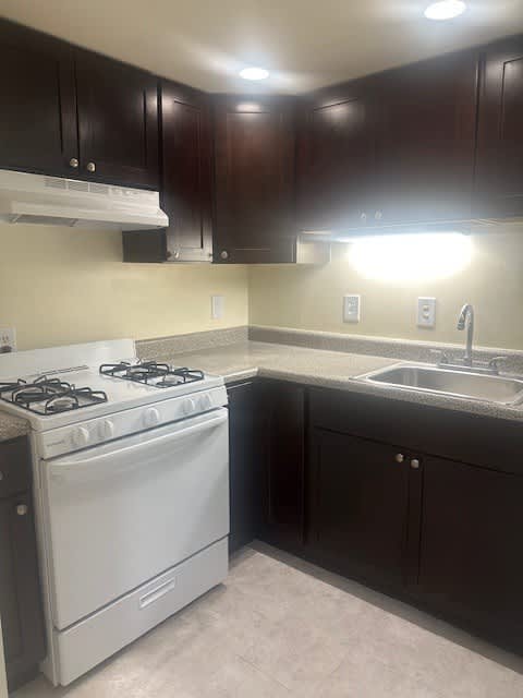 A white gas stove is in a kitchen with dark wood cabinets.
