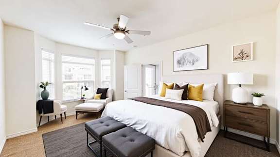 A bedroom with a large bed, a chair, a table, and a ceiling fan.