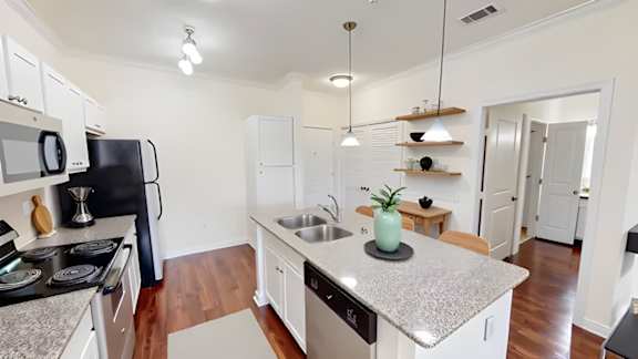 A kitchen with a black fridge, white cabinets, and a granite countertop.