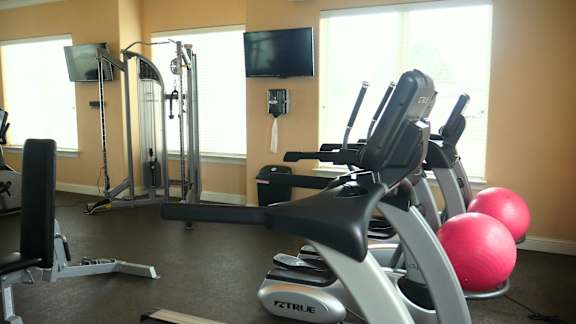A gym with a variety of equipment including a rowing machine, a stationary bike, a treadmill, a weight bench, and a television.