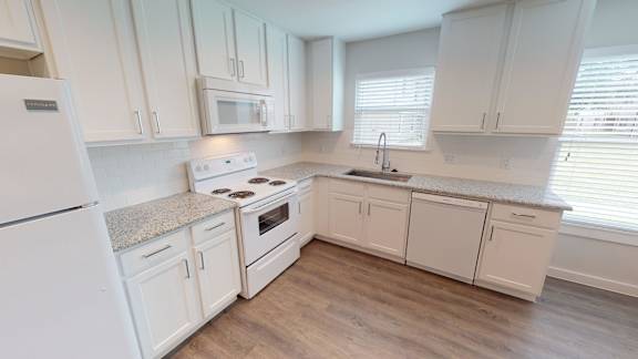 Floor Plan  A white kitchen with wooden floors and white appliances.