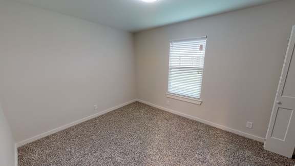 A room with a carpeted floor and a window with blinds.