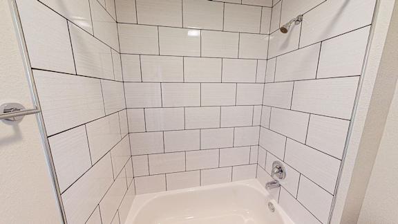 A white tiled shower with a white tub and a shower head.