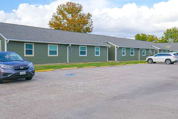 A parking lot with a blue car and a white car parked in front of a building with green siding.