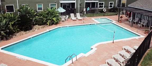 A rectangular pool surrounded by a concrete patio and a black fence.