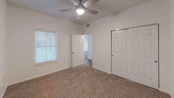 A room with a carpeted floor, a ceiling fan, and a window with blinds.