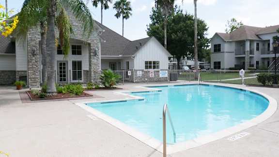 A swimming pool surrounded by palm trees and a building in the background.