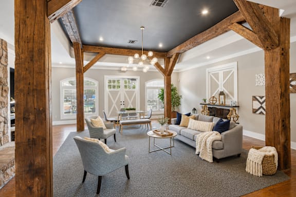 A living room with a grey couch, a grey chair, a wooden floor, and a wooden beam ceiling.