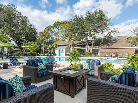 A sunny day at the poolside with wicker chairs and tables. at Parkland at Orange Park Apartments , Orange Park, FL, 32073