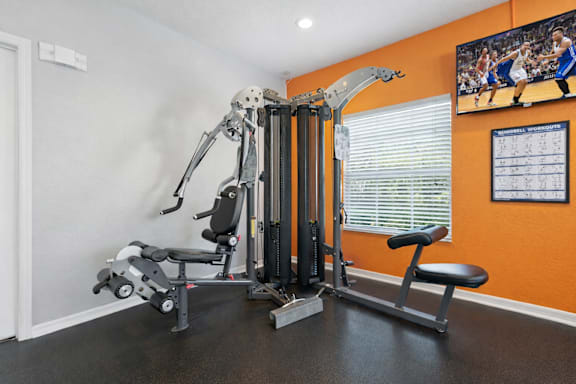 A home gym with a weight machine, a bench, and a television screen showing a basketball game. at Waterbridge Apartments , Orlando, Florida