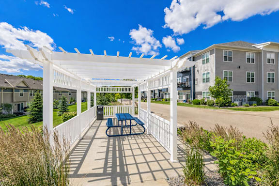 A white pergola with a bench is in the foreground of a residential area.