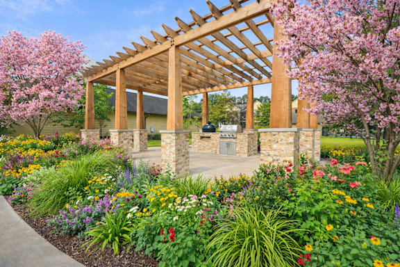 A wooden pergola stands over a garden with a stone wall and a pathway.