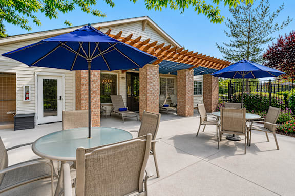 A patio with a table and chairs under blue umbrellas.
