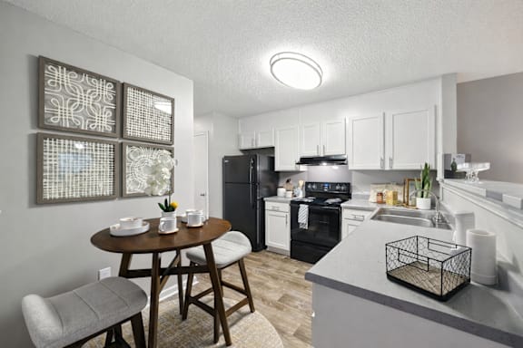 A kitchen with a table and chairs in the foreground and a refrigerator, oven, and sink in the background.