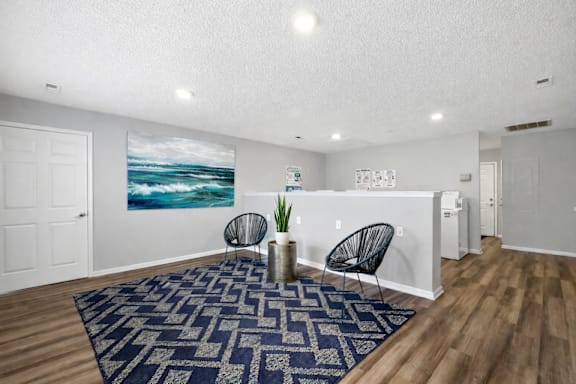 A room with a blue rug and a painting of a beach scene on the wall.