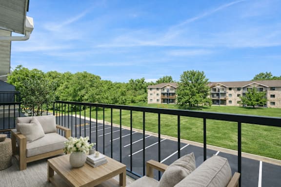 A balcony with a table and chairs overlooking a parking lot and apartment buildings.