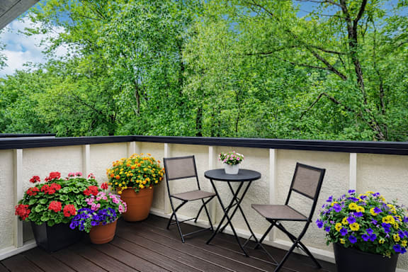 A balcony with a table and chairs overlooking a green forest.
