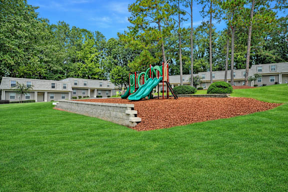 A playground with a green slide in the middle of a grassy area.
