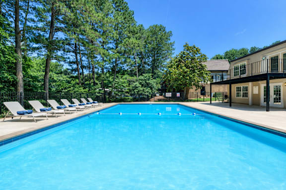 A large blue swimming pool surrounded by trees and lounge chairs.