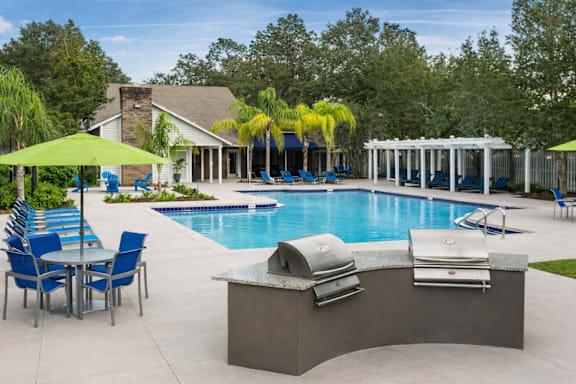 A pool with a table and chairs and a sun shade. at Parkland at Orange Park Apartments , Orange Park, FL, 32073