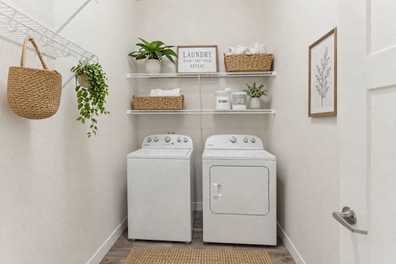 A laundry room with a washer and dryer, a basket, a plant, and a sign.
