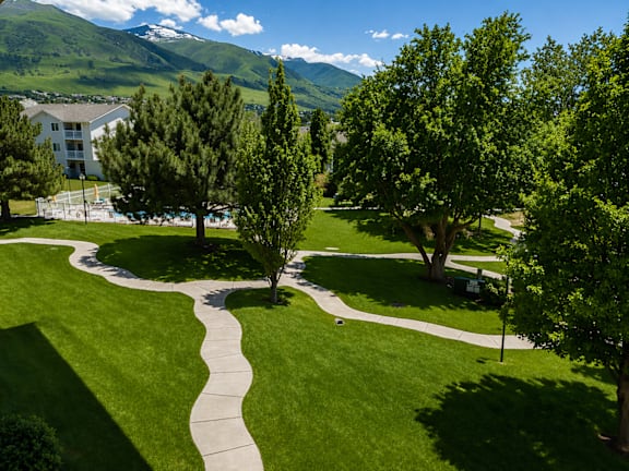 A pathway leads through a grassy area with trees and a mountain in the background.