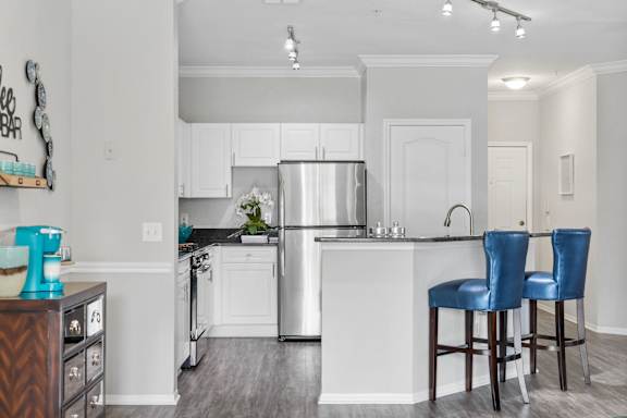 A kitchen with a refrigerator, sink, and two blue barstools.