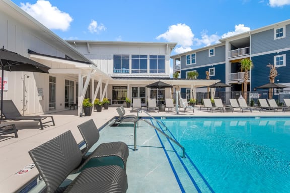 a swimming pool with lounge chairs and umbrellas in front of a building at Bristol at New Riverside, Bluffton, SC 29910