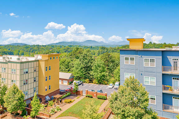 A view of a hotel with a parking lot in front and a mountain in the background at The Lofts at Reynolds Village Apartments, Asheville, North Carolina