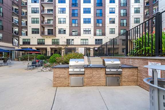 A patio with barbecue grills and a building in the background.