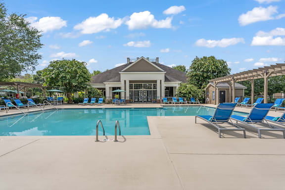 a resort style pool with lounge chairs and a clubhouse in the background