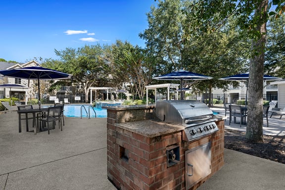 an outdoor patio with a barbecue grill and tables with umbrellas