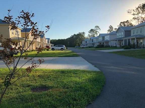 A white car is parked on the street in front of a house.