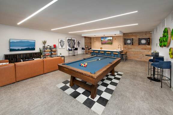 A pool table is in the middle of a room with a bar and a television.